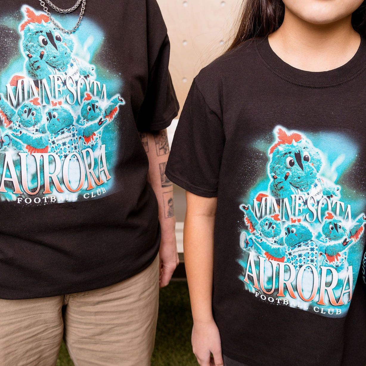 Two people wearing black t-shirts with a colorful graphic design, standing next to soccer balls.