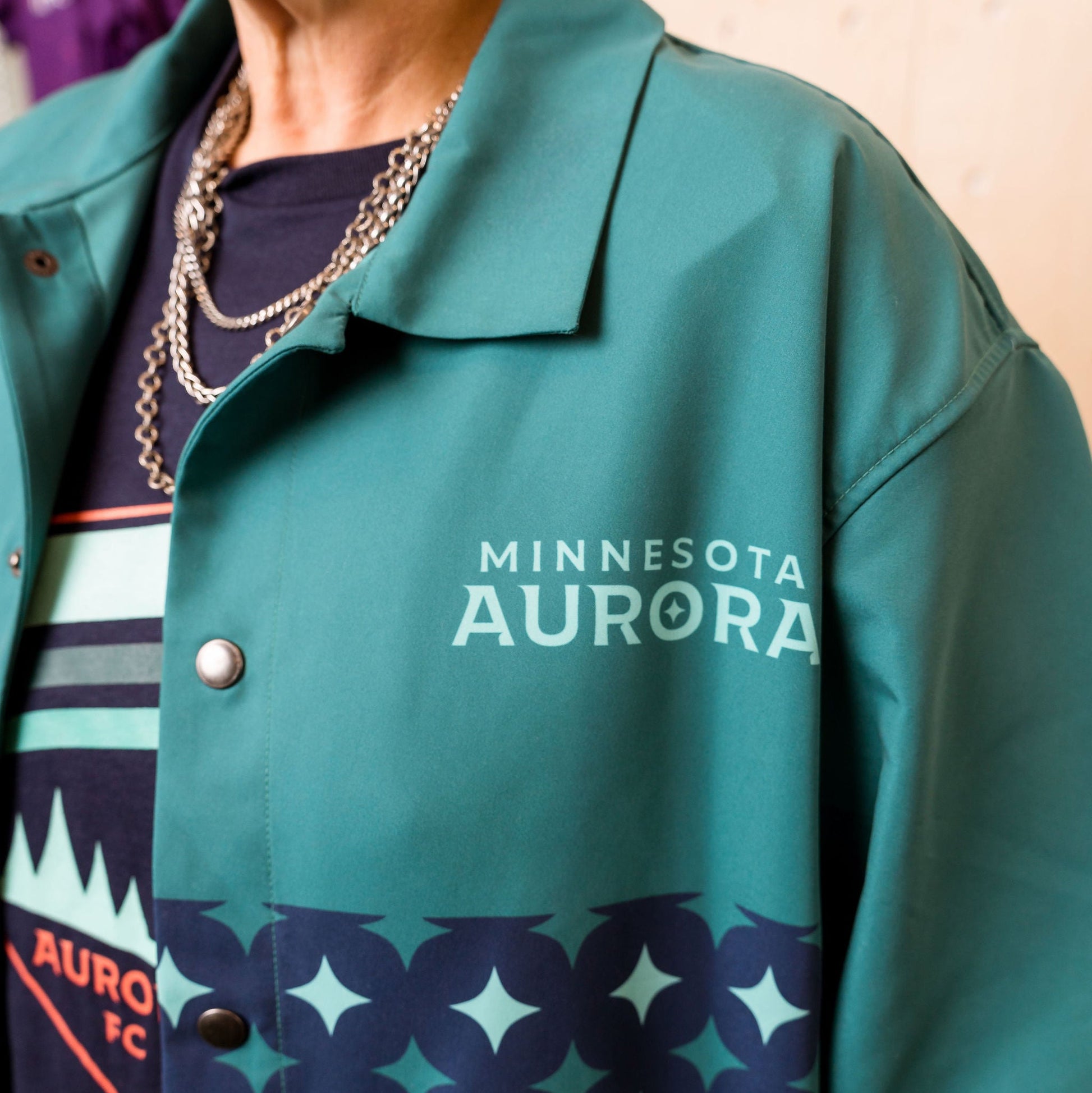 Teal jacket with 'Minnesota Aurora' text on a person wearing a dark shirt.