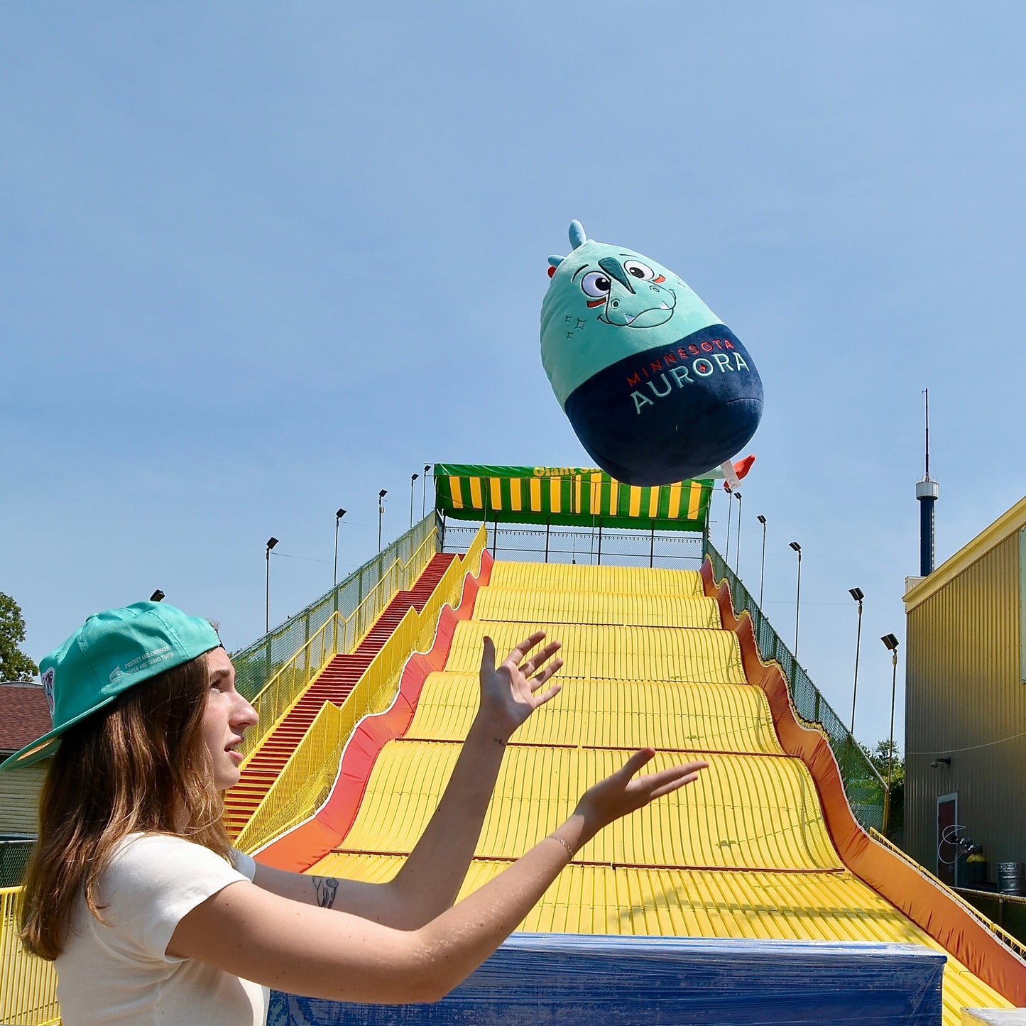 Woman throwing a Rory Squishie Pillow in front of the big slide at the State Fair.