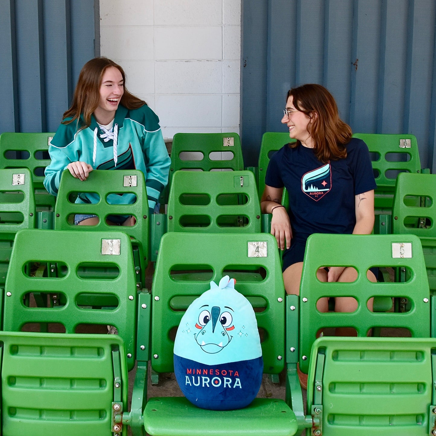 Two people sitting on green chairs with a Rory Squishie Pillow.