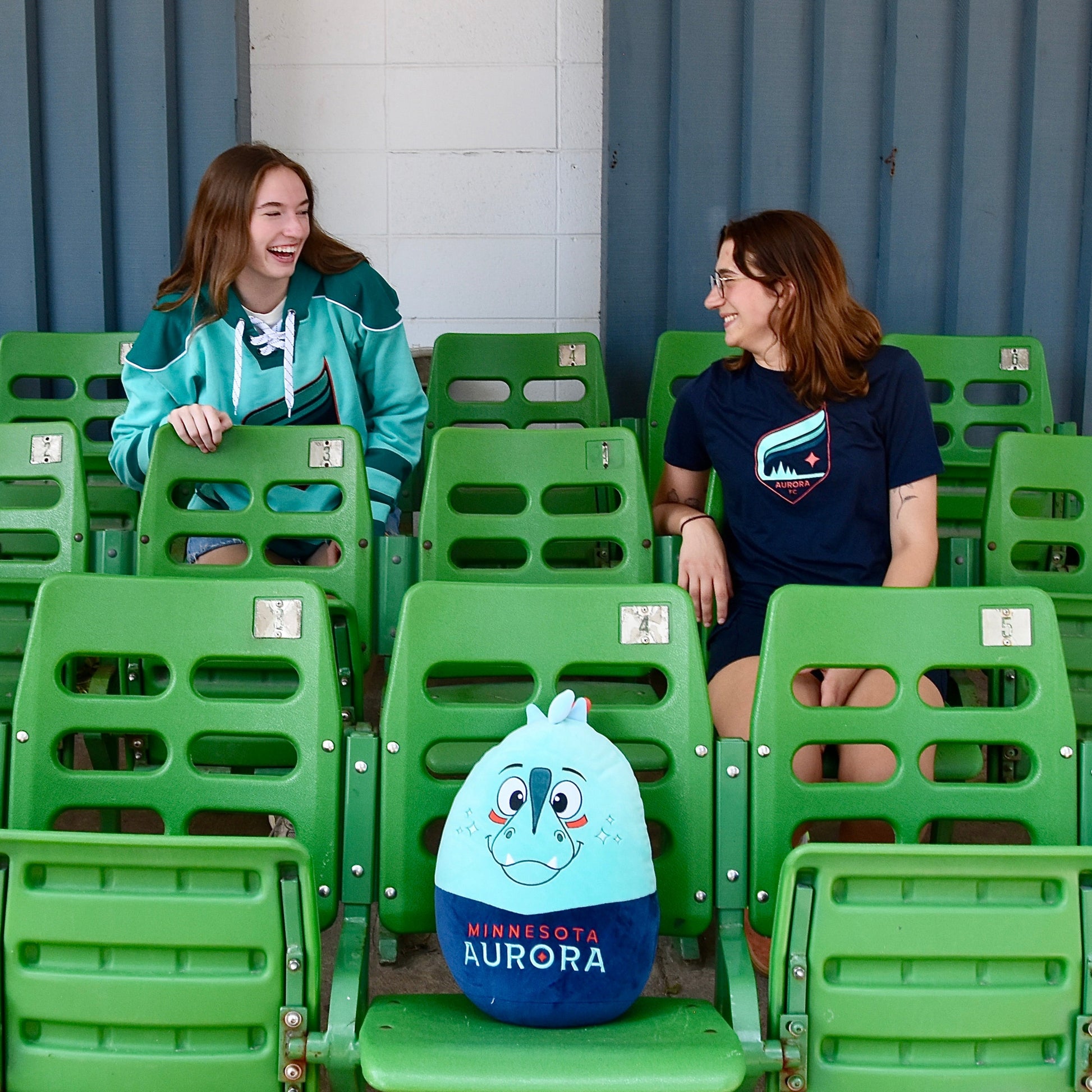 Two people sitting on green chairs with a Rory Squishie Pillow.