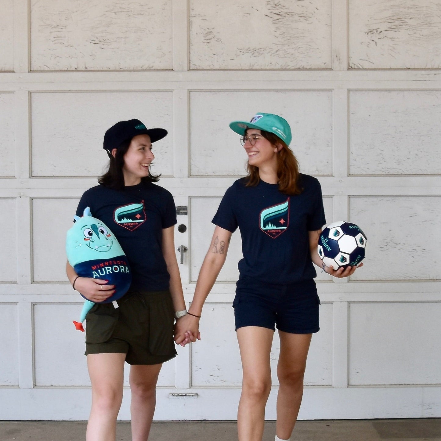 Two people walking side by side holding soccer ball and a Rory Squishie pillow in front of a garage door.