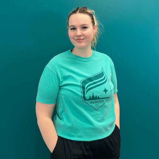 Person wearing a teal t-shirt with a logo against a teal background