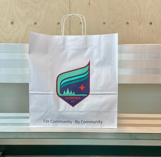 White paper bag with Aurora FC logo on a wooden surface