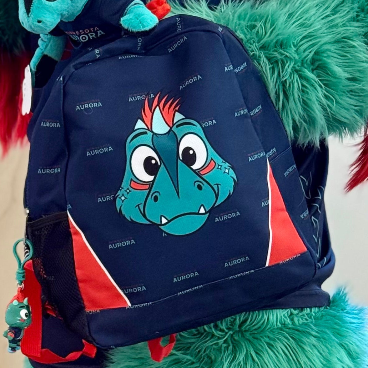 Navy blue backpack with some accents of orange featuring the face of the Aurora mascot, Rory the Aurorasaurus