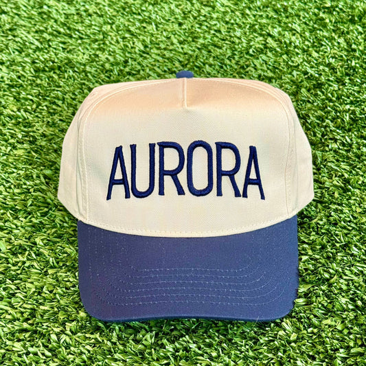 Trucker hat with navy 'AURORA' on a green grass background