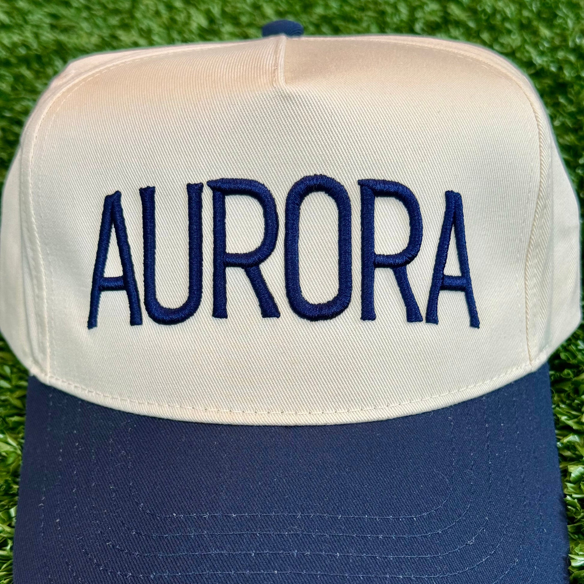 close up of embroidered Cap with 'AURORA' embroidered on it, placed on grass.