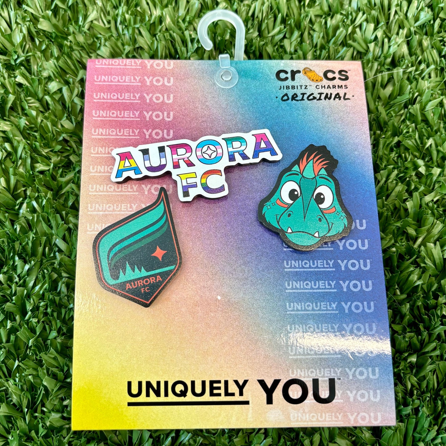 Aurora Croc Jibbitz Charms on a colorful card with Crocs branding, placed on grass.