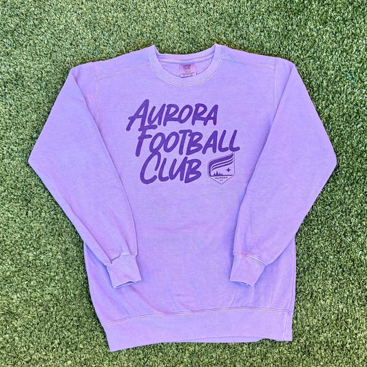 Purple sweatshirt with 'Aurora Football Club' text on a grassy surface