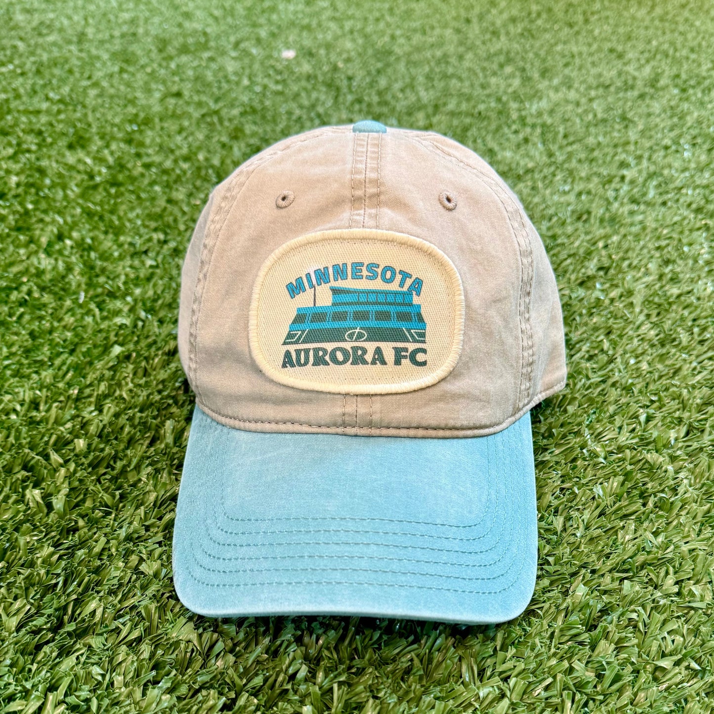 Cap with Minnesota Aurora FC logo on a grassy surface