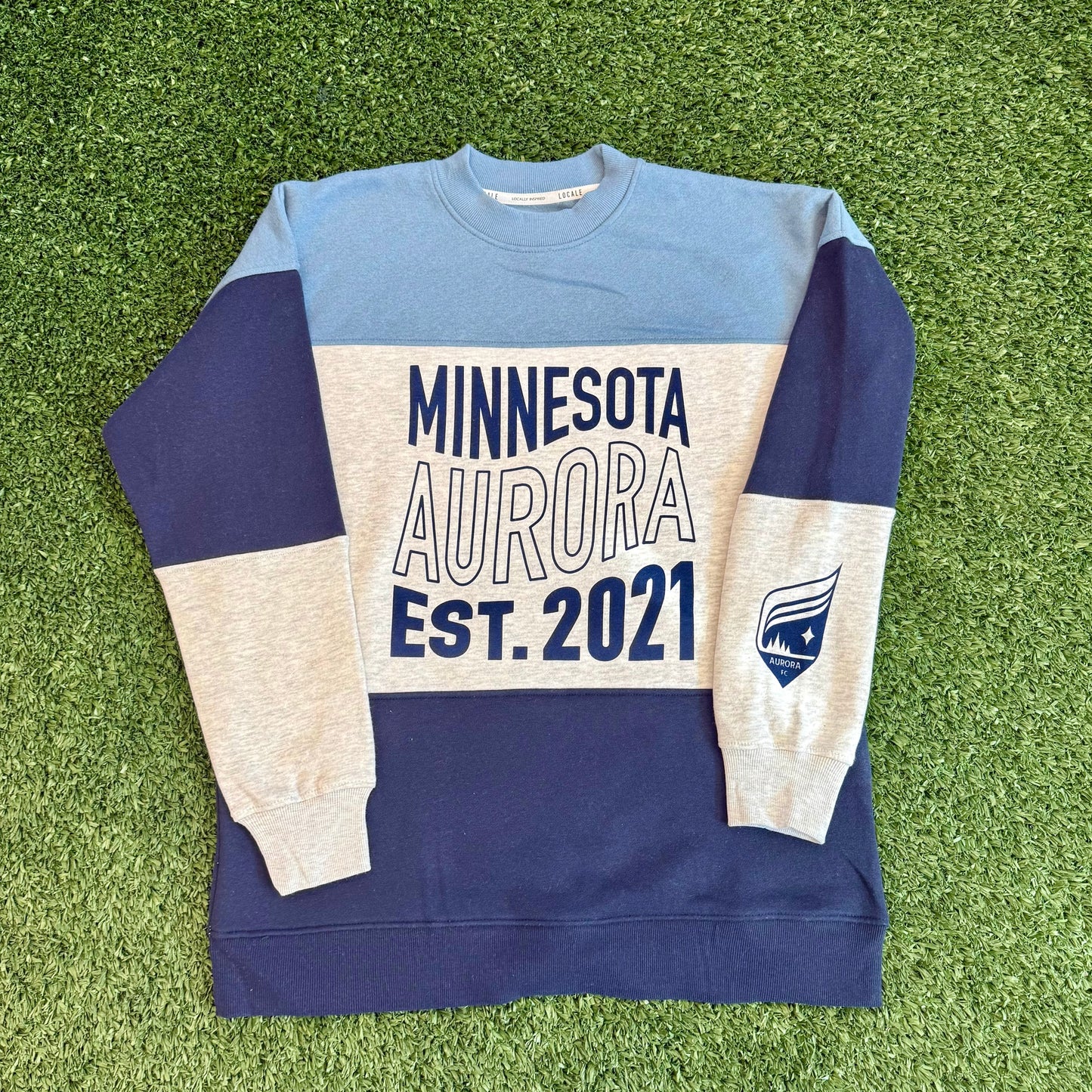 Sweatshirt with 'Minnesota Aurora Est. 2021' text on a grassy surface