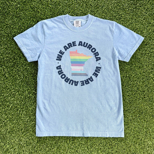 Light blue t-shirt with 'We Are Aurora' graphic on a grass background