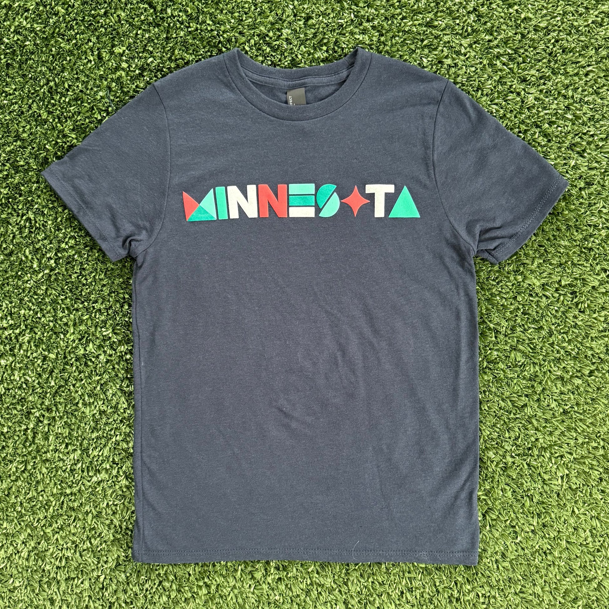 Navt t-shirt with 'MINNESOTA' printed on it laid flat on green grass.