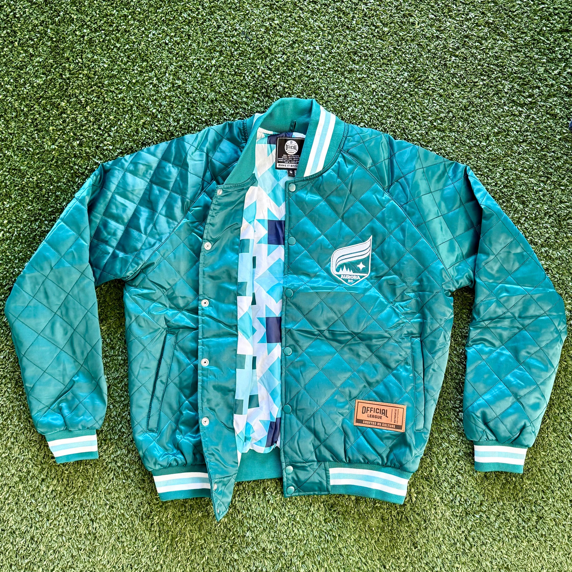 Teal jacket with plaid lining on a green grassy surface