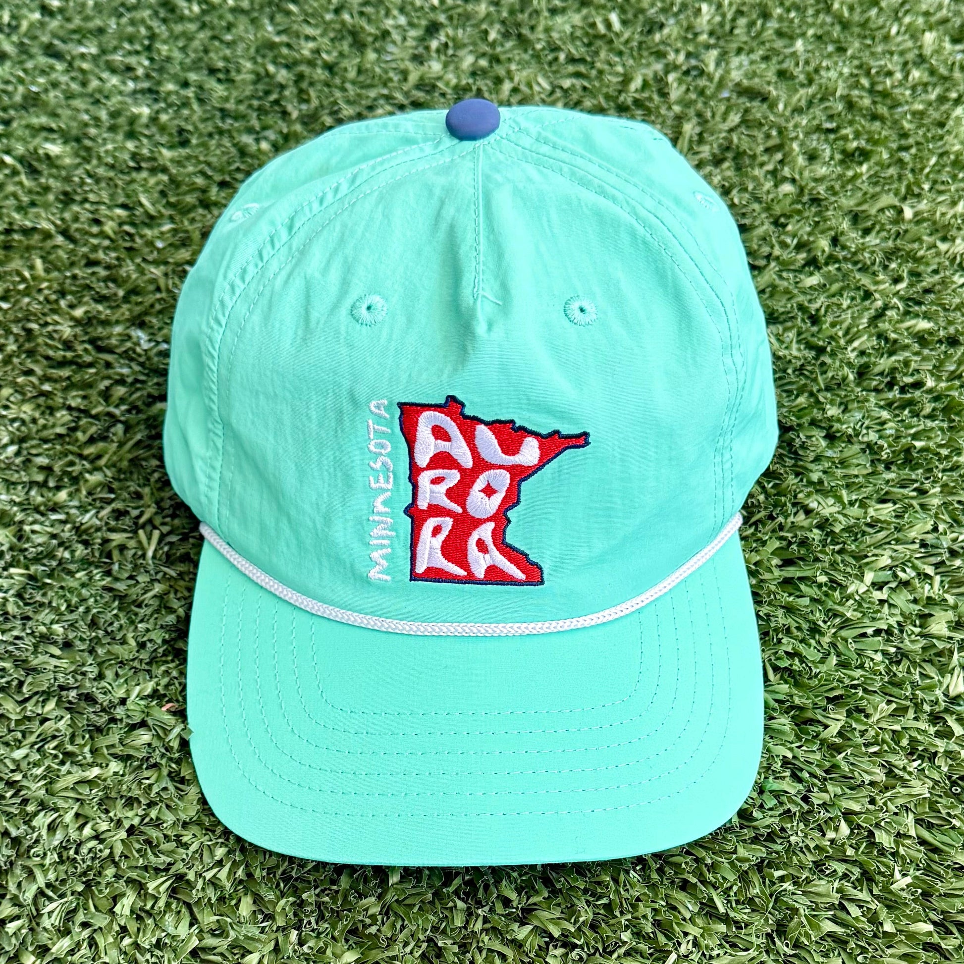 Light teal cap with a MN logo on a grassy background