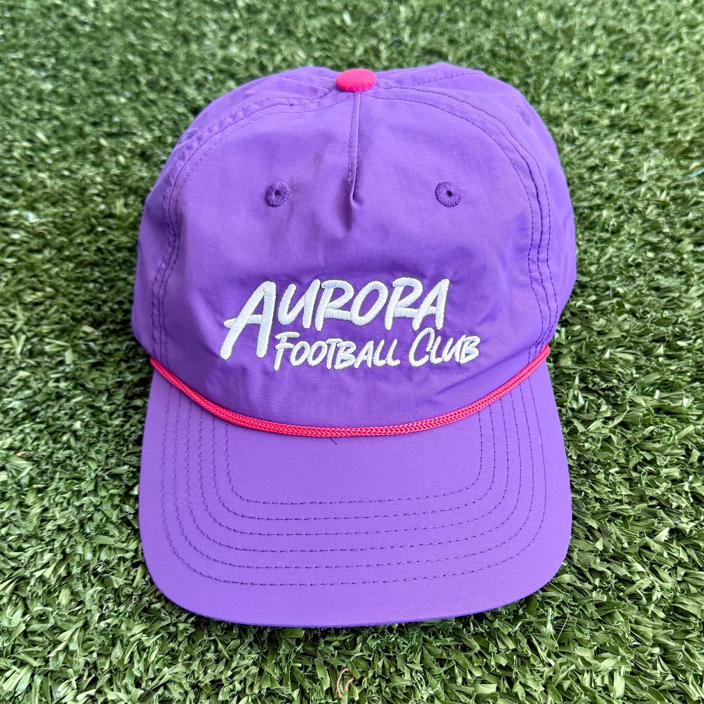 Purple cap with 'Aurora Football Club' text on a grassy background
