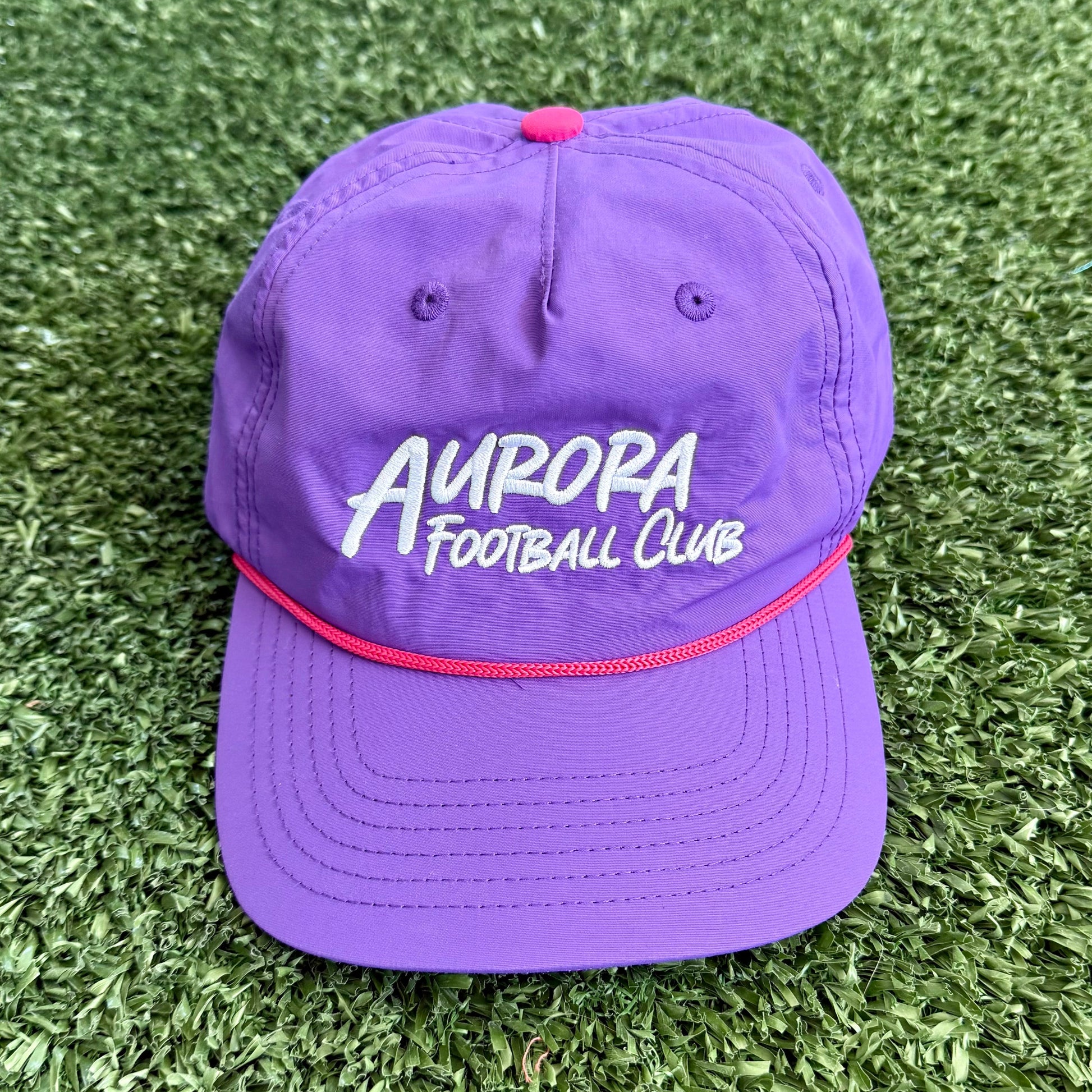 Purple cap with 'Aurora Football Club' text on a grassy background