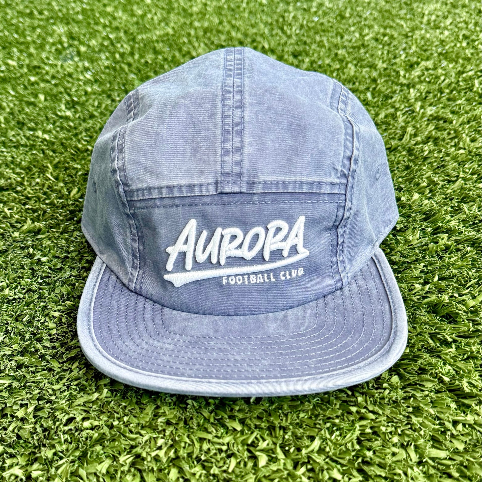 Denim hat with 'Aurora' text on a turf surface