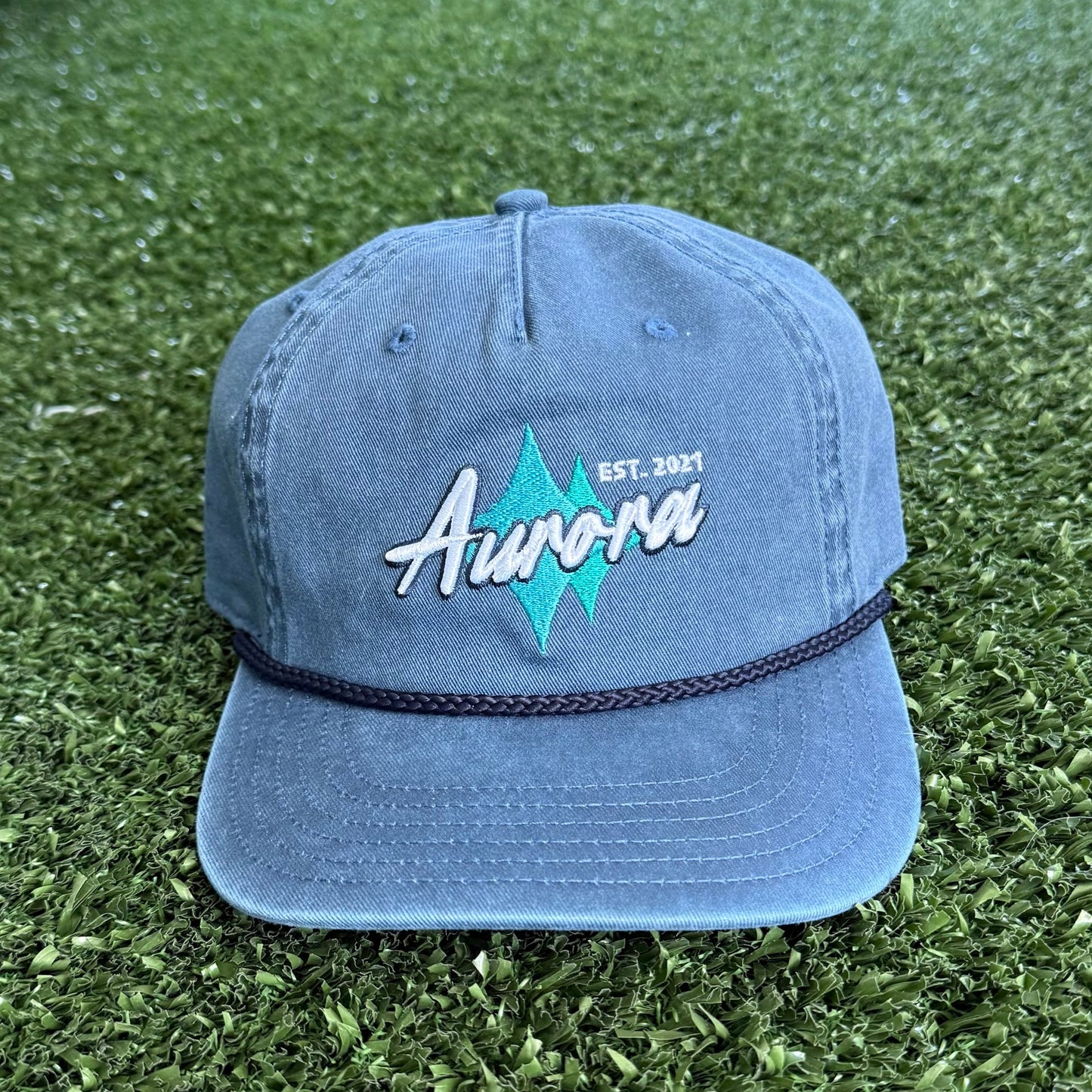 Blue cap with 'Aurora' logo on a green grassy surface