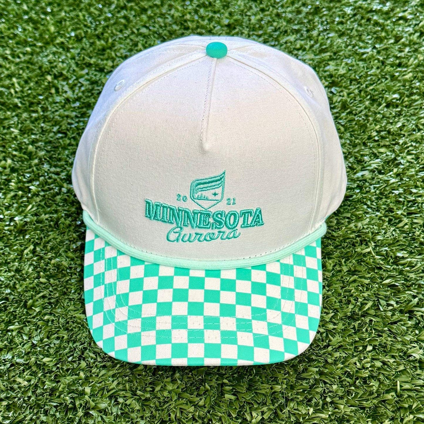 White and teal checkered cap on a green grass-like surface