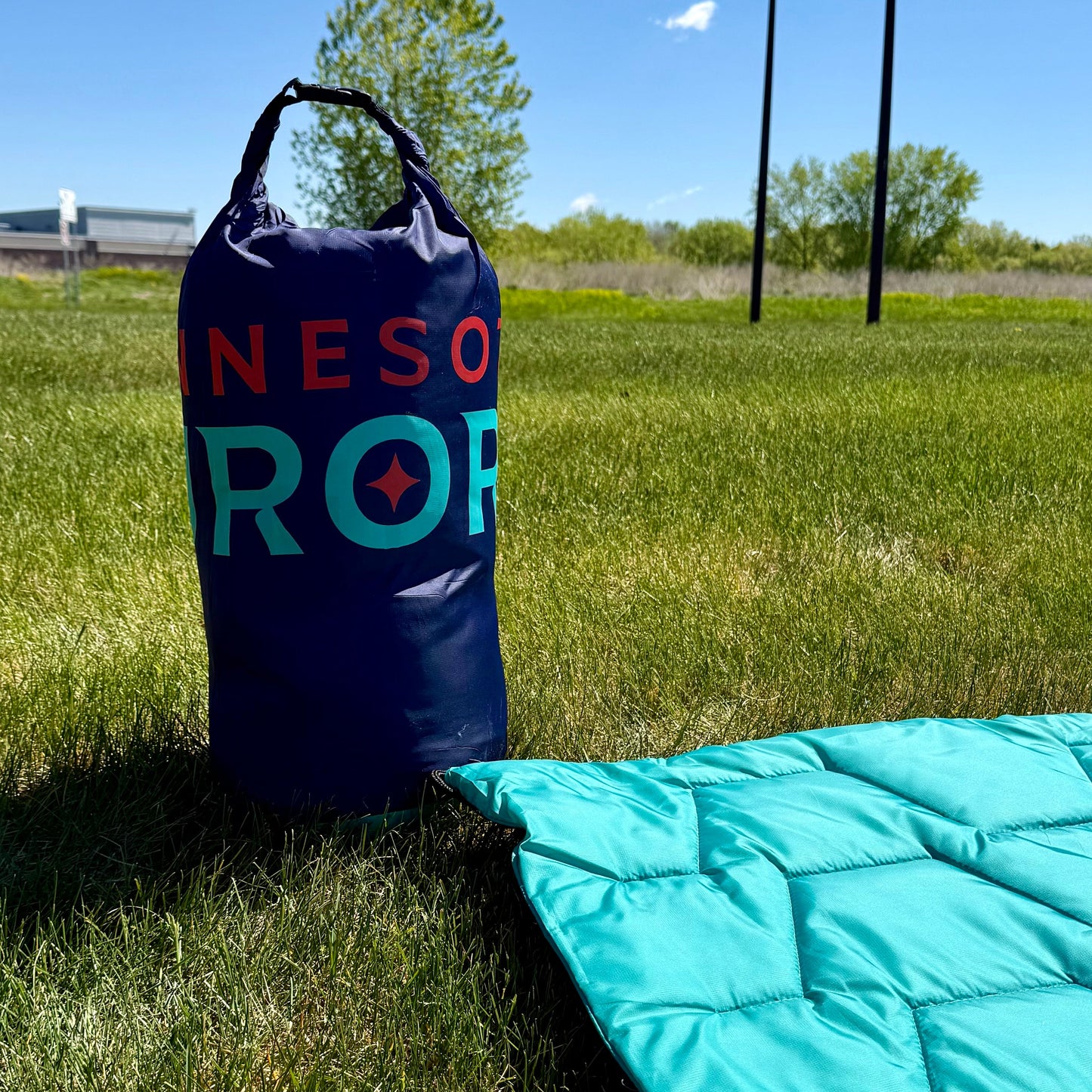 Navy blanket storage bag  labeled "Minnesota Aurora" on grass with a teal blanket nearby