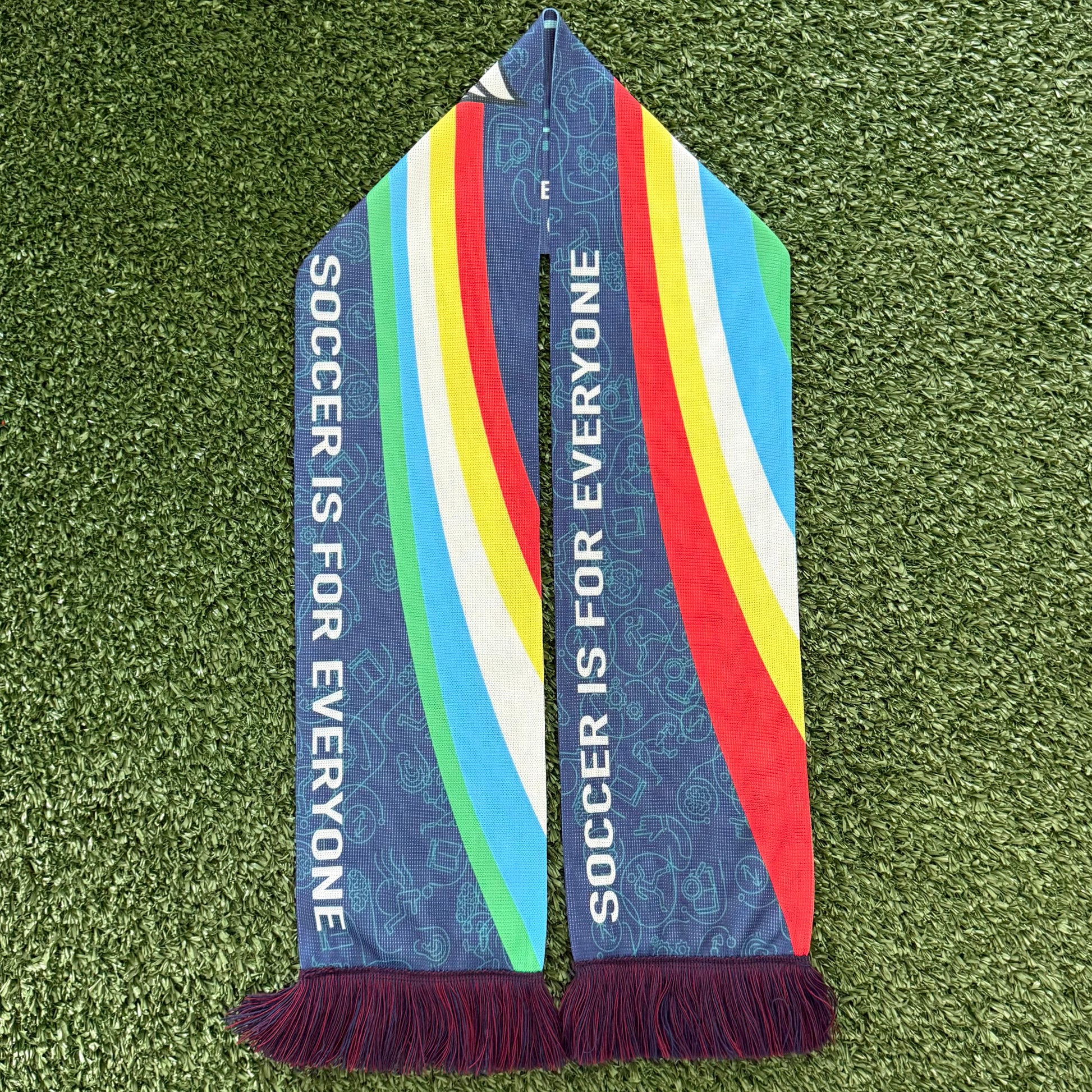 Colorful Disability Awareness scarf with 'Soccer is for Everyone' text on a green grass background