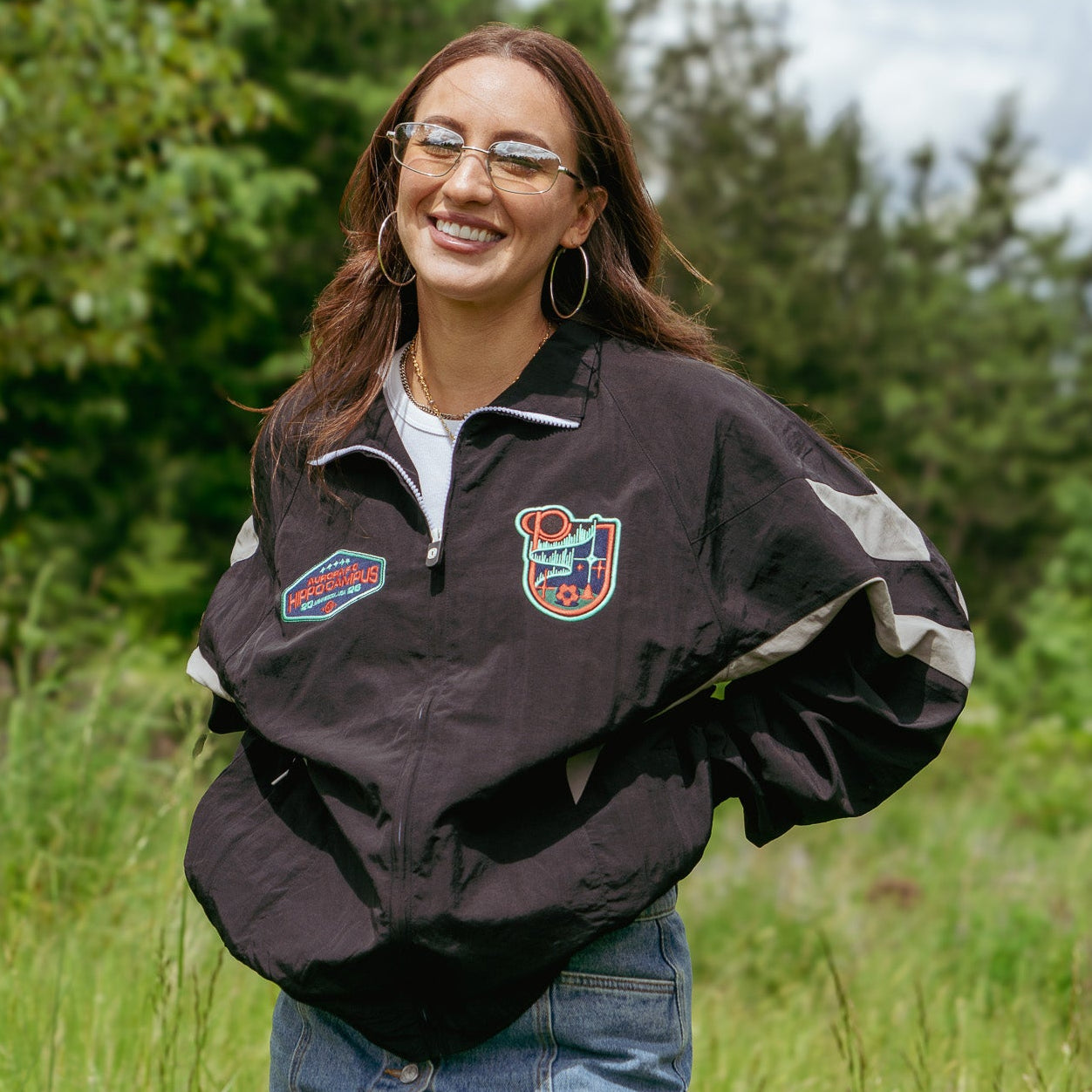 Person wearing a black jacket with patches in a grassy outdoor setting