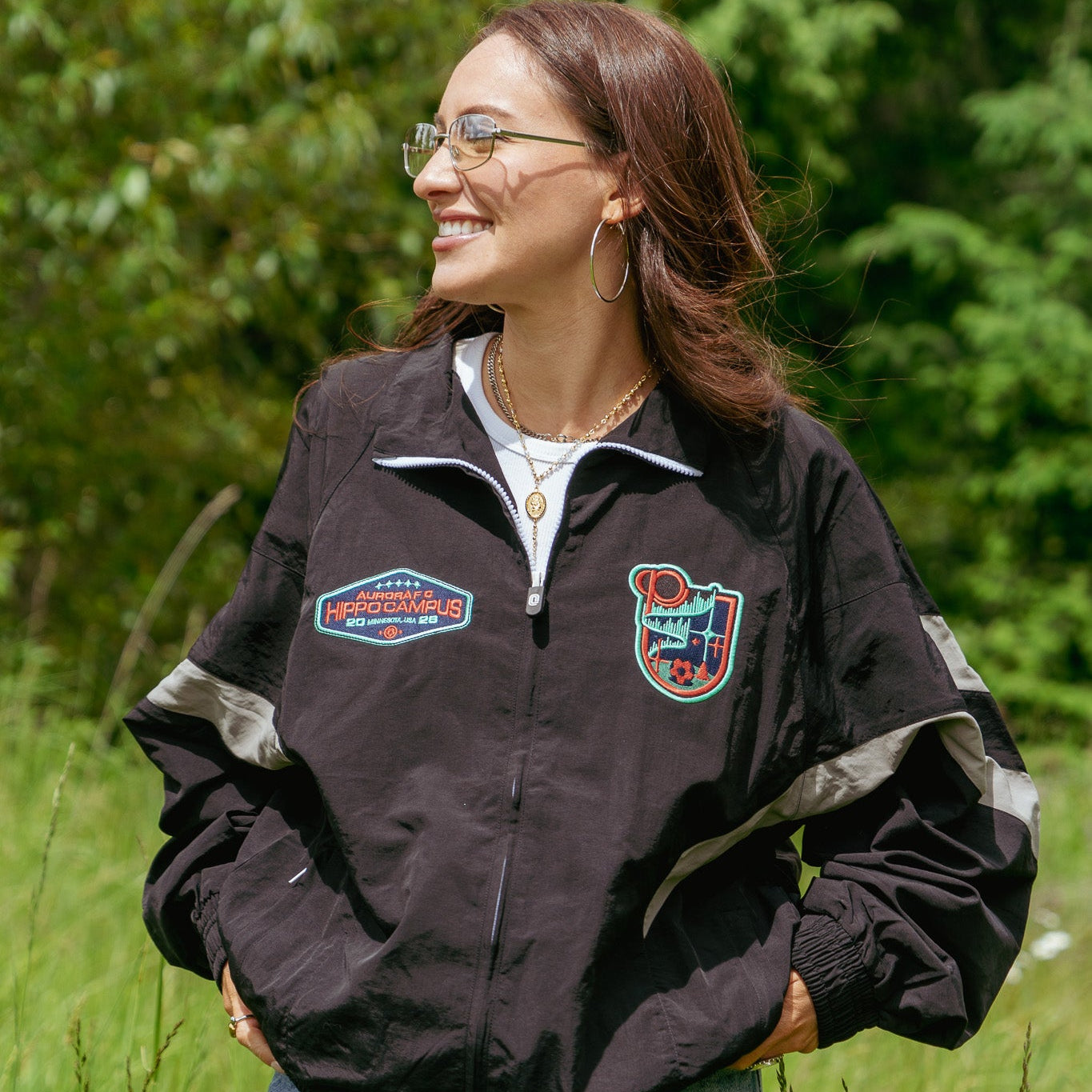 Woman wearing a black jacket with logos in a grassy outdoor setting