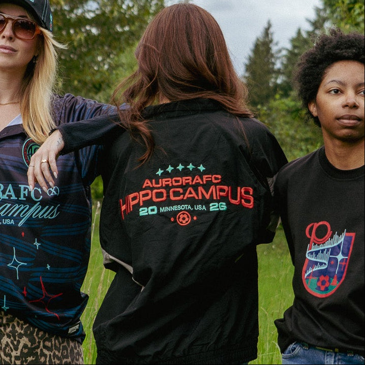 Three people standing in a grassy field wearing black t-shirts with visible text and graphics.