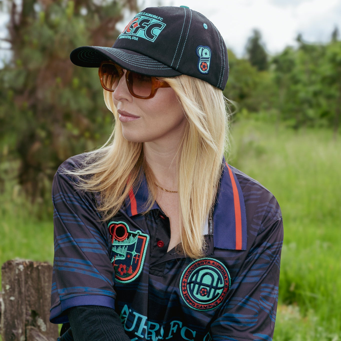 Woman wearing a cap and jacket with logos in a natural setting