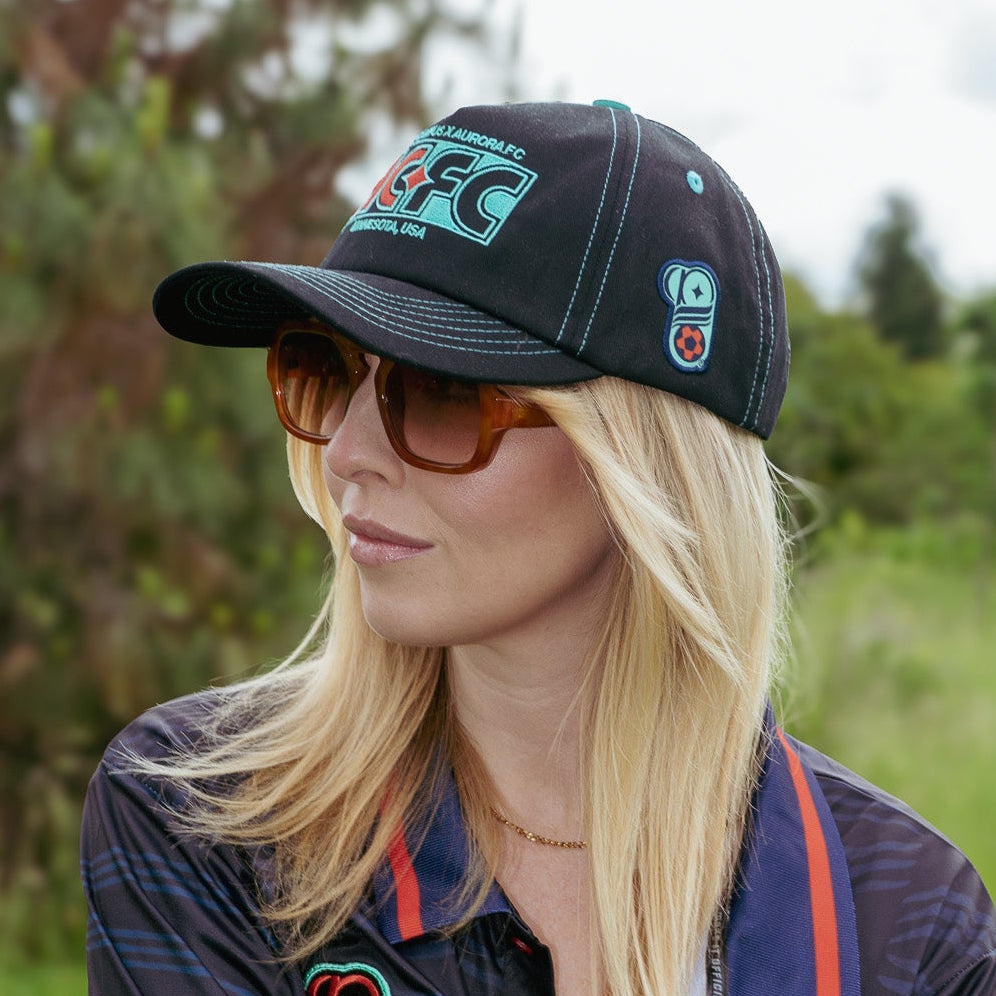 Woman wearing a cap and jacket with logos in a natural setting