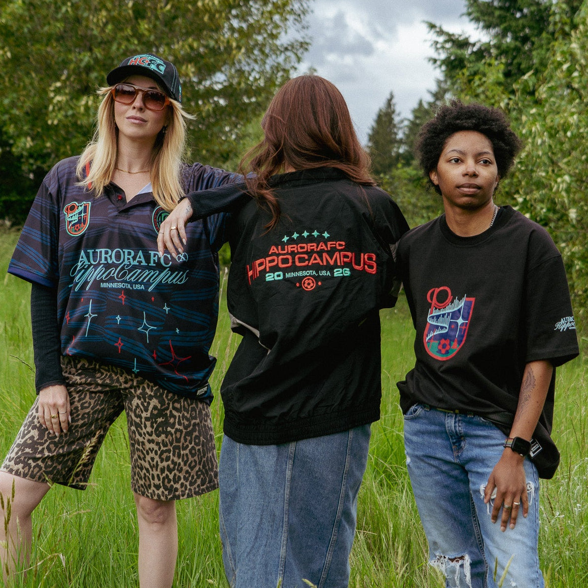 Three people standing in a grassy field wearing black t-shirts with visible text and graphics.