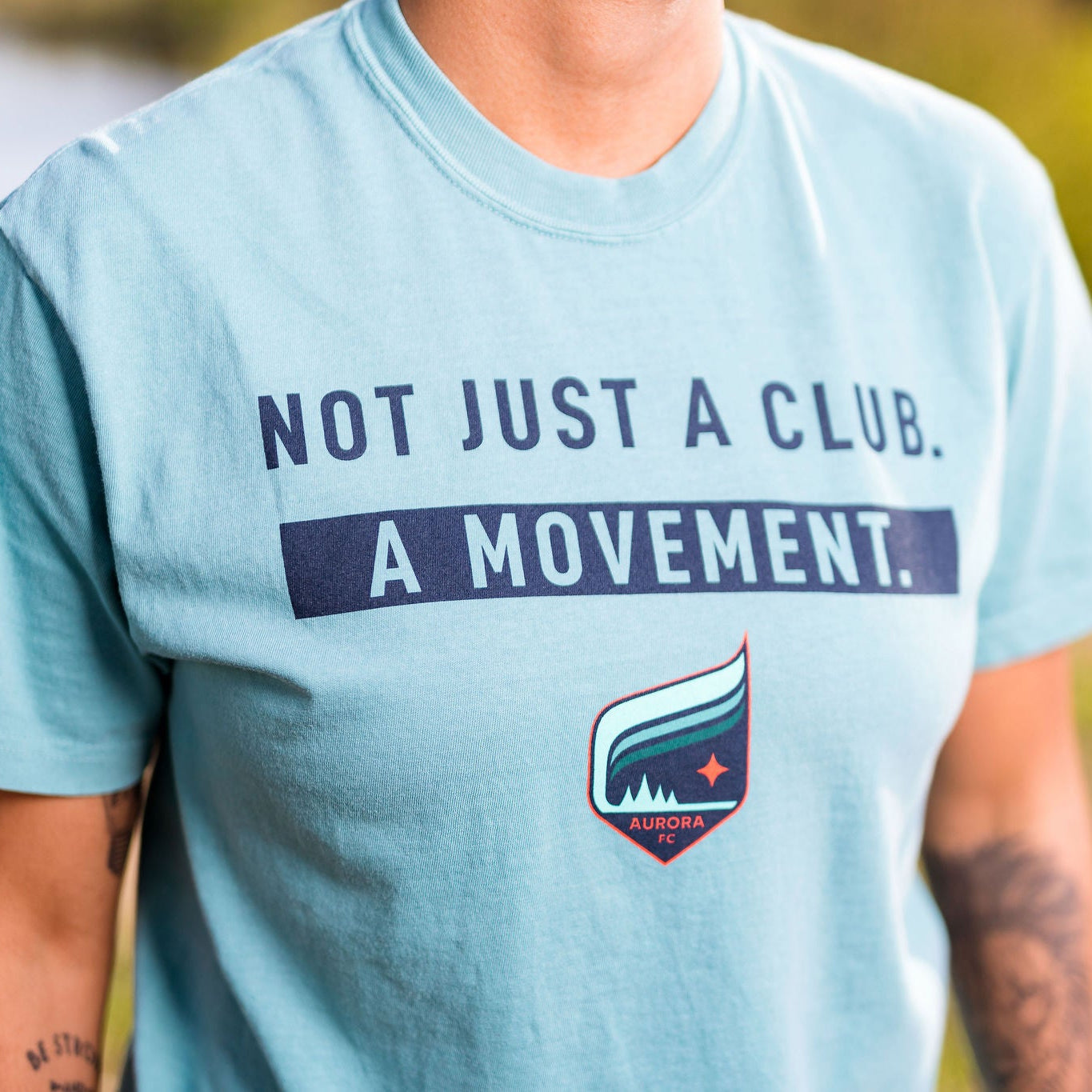 Person wearing a teal t-shirt with 'Not Just a Club, A Movement' text and logo.