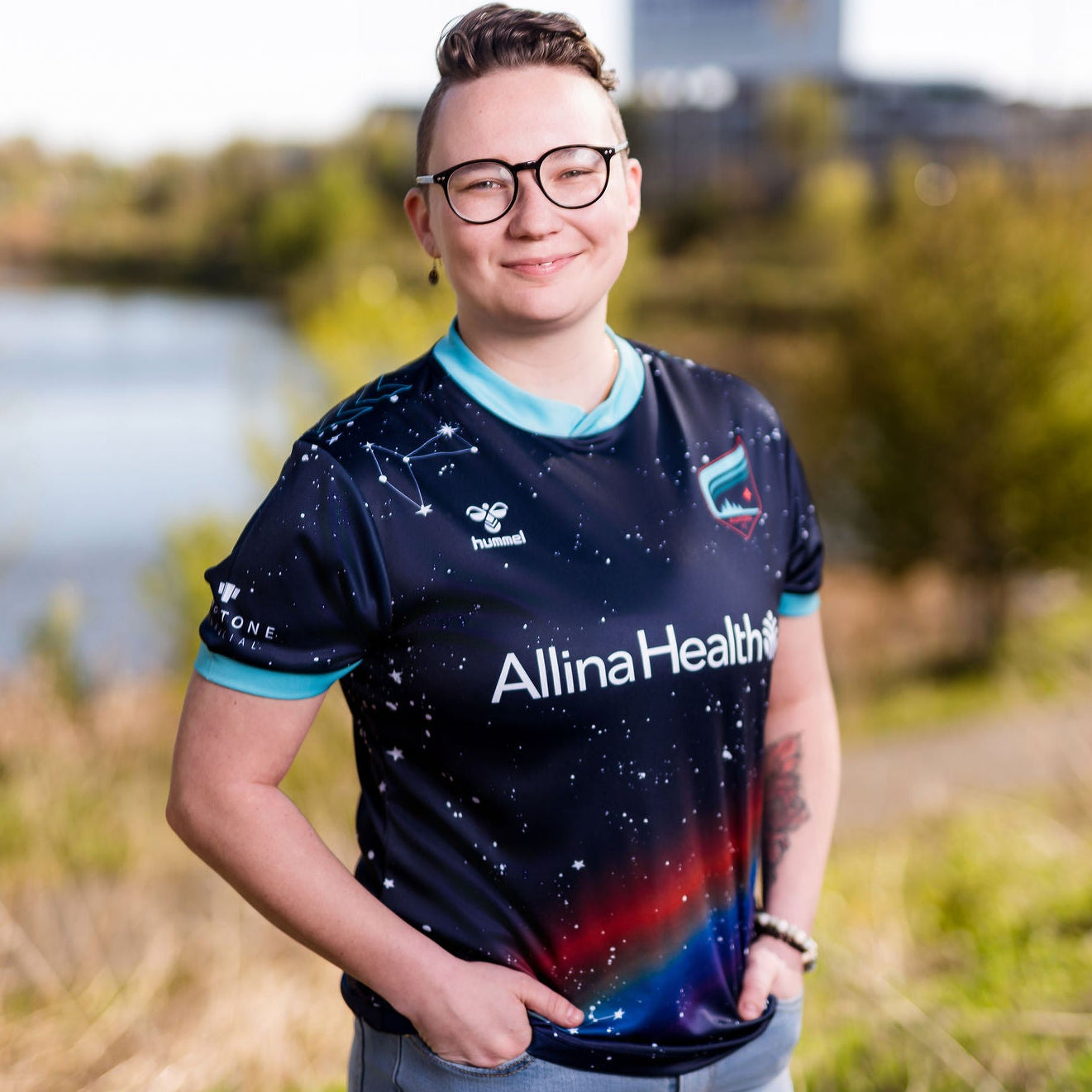 Person wearing a pride sports jersey with 'Allina Health' branding outdoors.