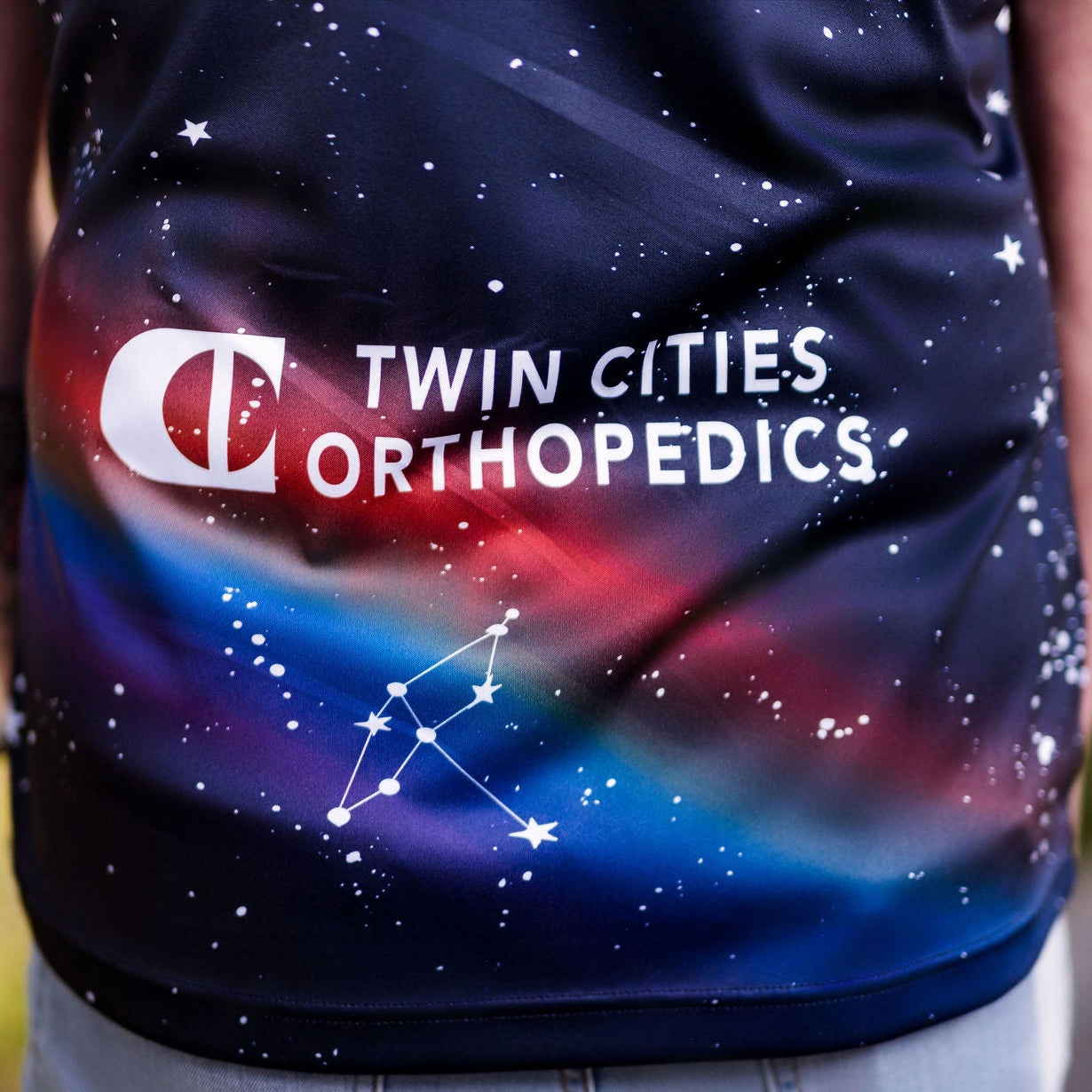 Person wearing a shirt with 'Twin Cities Orthopededics' logo and space-themed design.