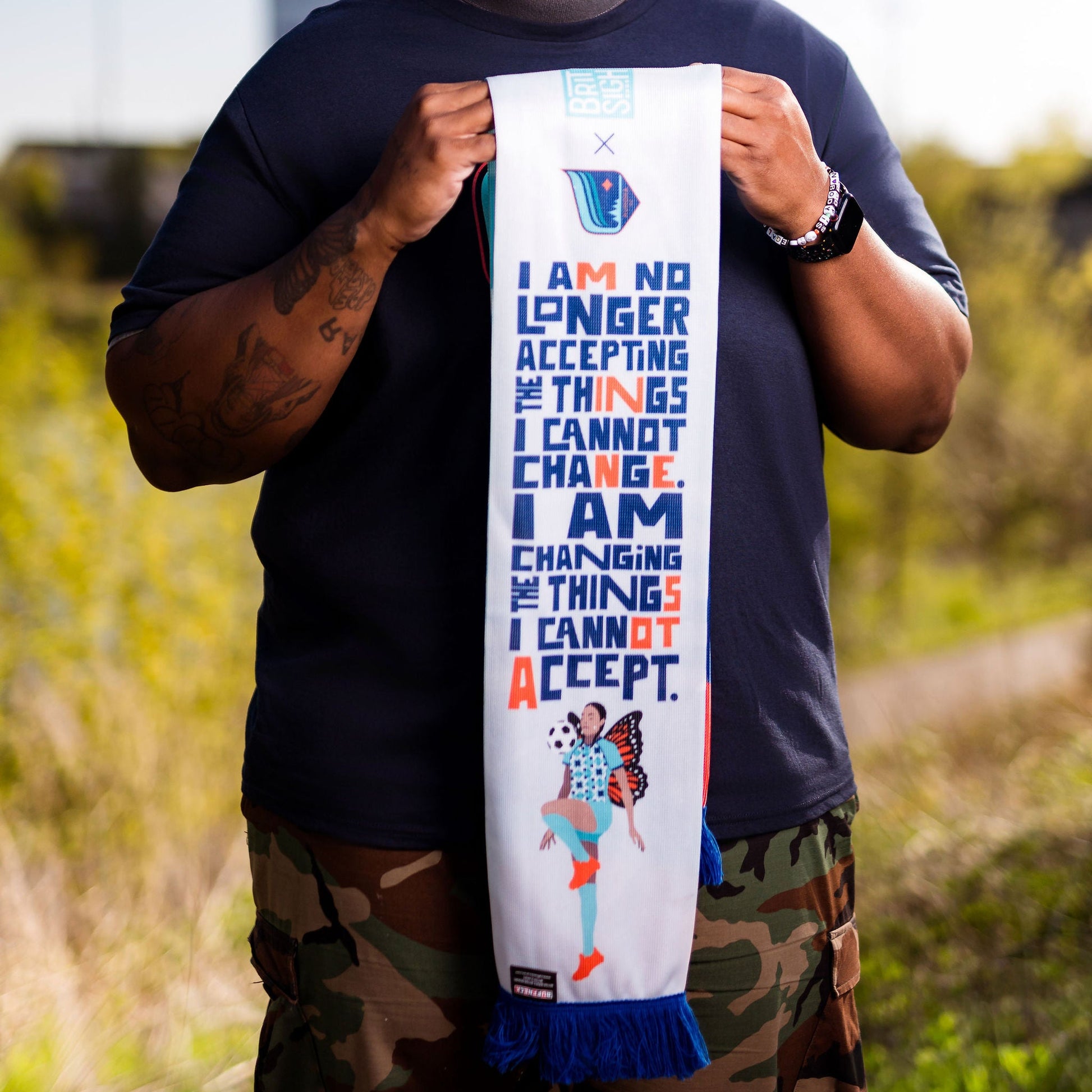 Man holding a colorful scarf with motivational text outdoors
