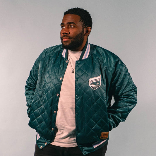 Man wearing a green quilted jacket with a logo on a white background