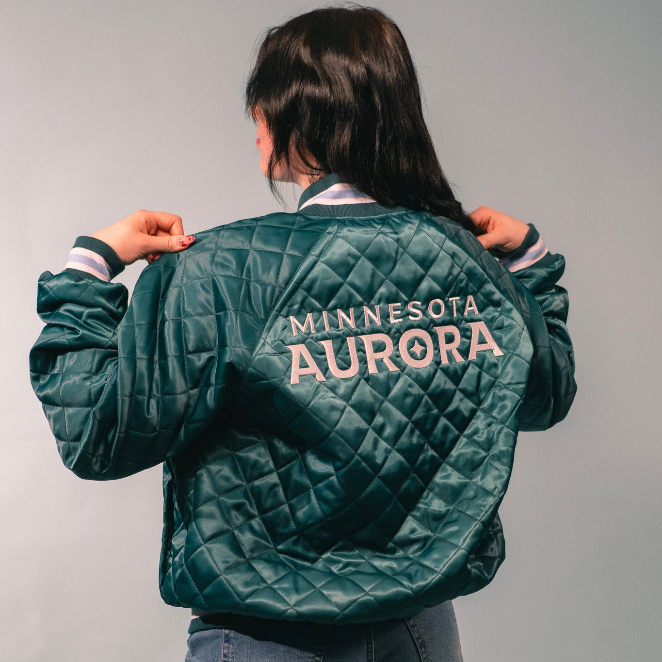 Person wearing a green quilted jacket with 'Minnesota Aurora' text on the back against a gray background