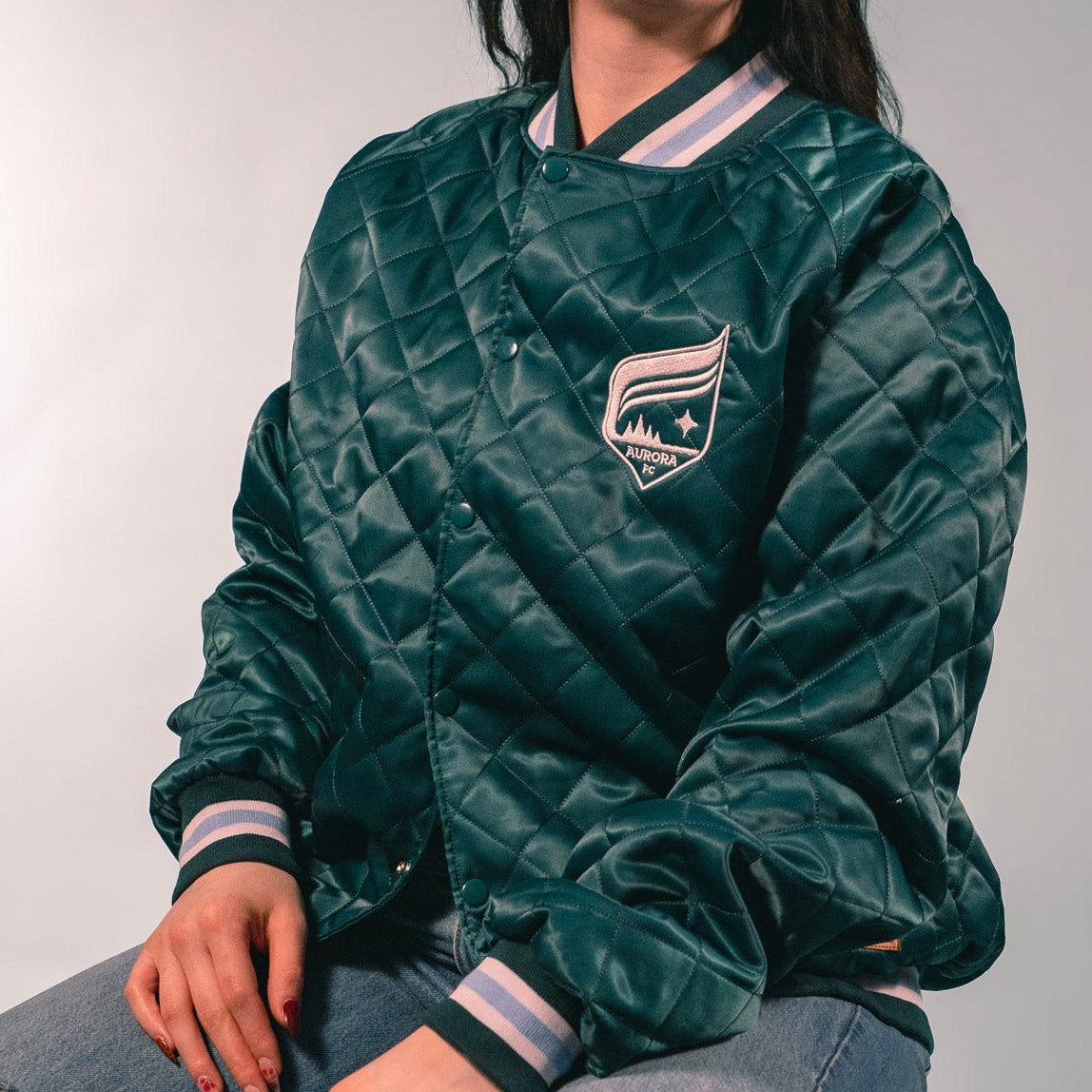 Person wearing a green quilted jacket with a logo, sitting against a plain background