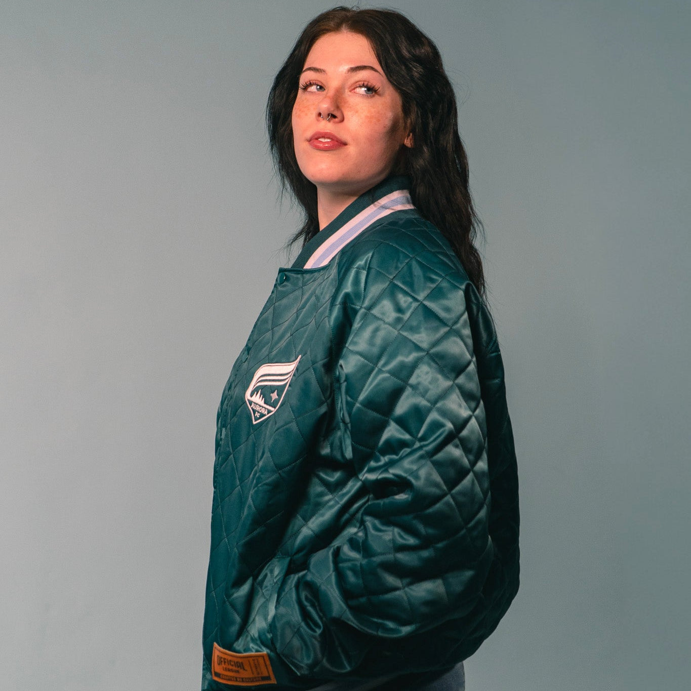 Person wearing a green quilted jacket with a logo on a gray background