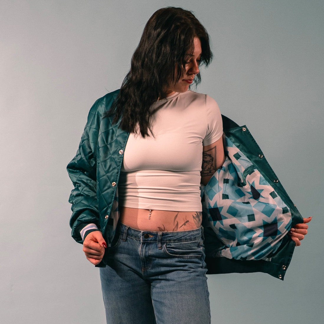 Person holding a green jacket with a quilted teal pattern on a gray background